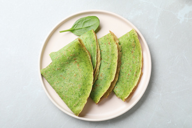 Tasty spinach crepes on light grey marble table, top view