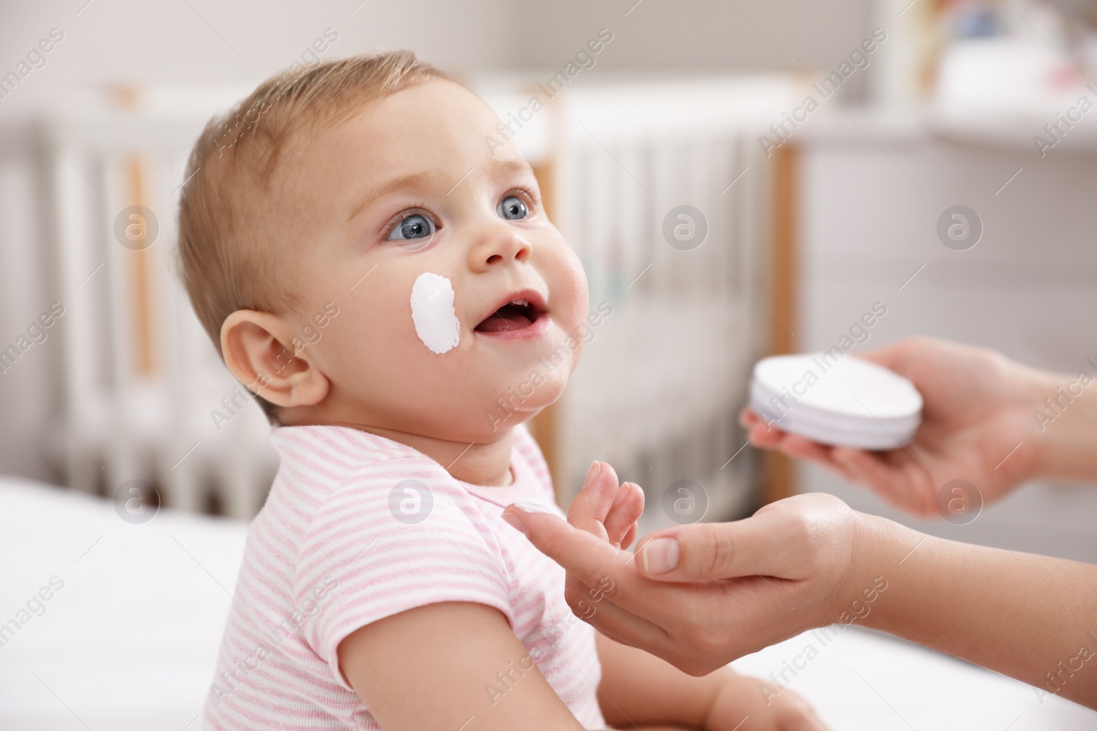 Photo of Mother applying moisturizing cream on her little baby at home, closeup