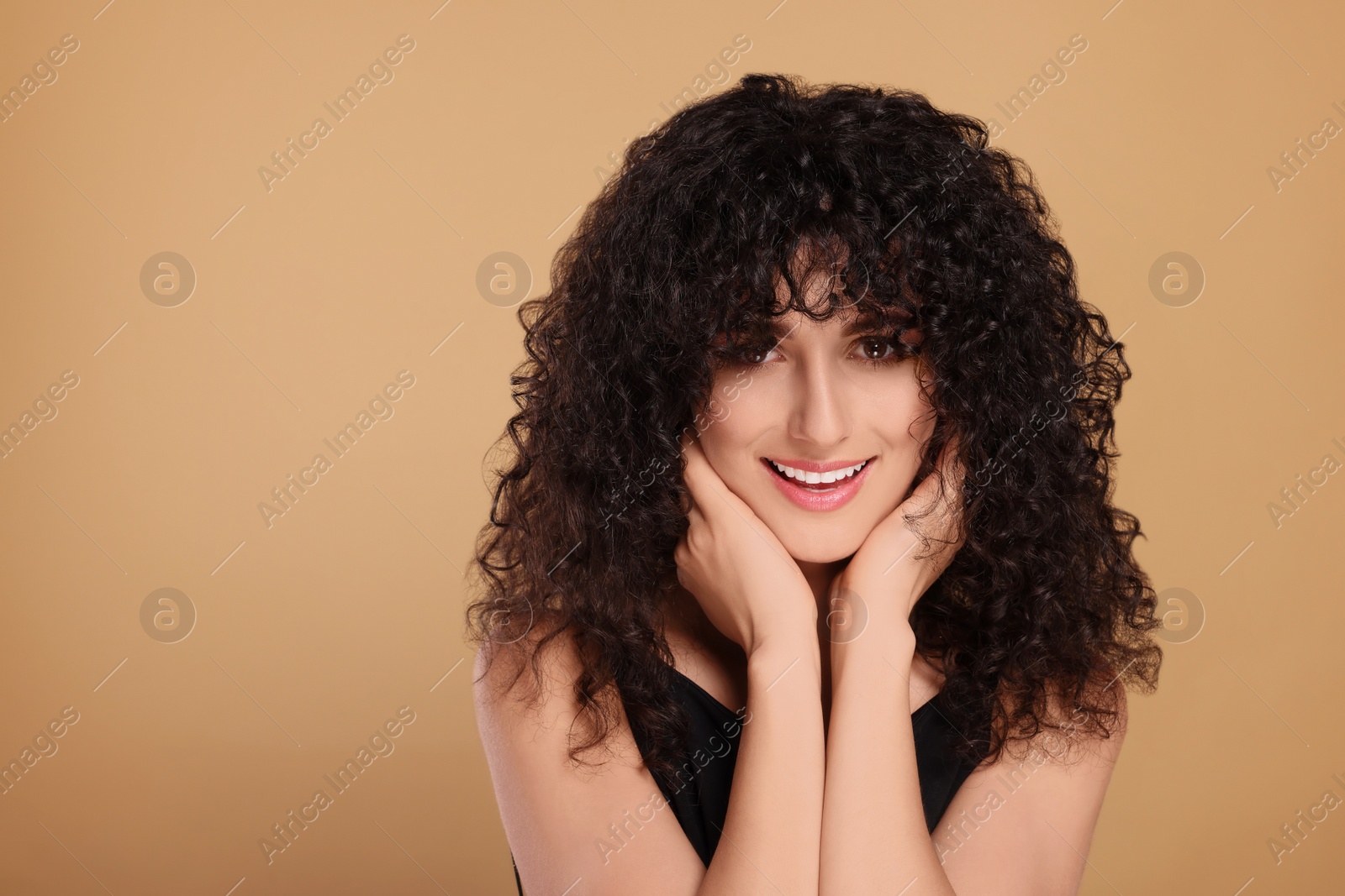 Photo of Beautiful young woman with long curly hair on beige background. Space for text