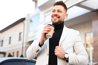 Businessman with cup of coffee on city street in morning