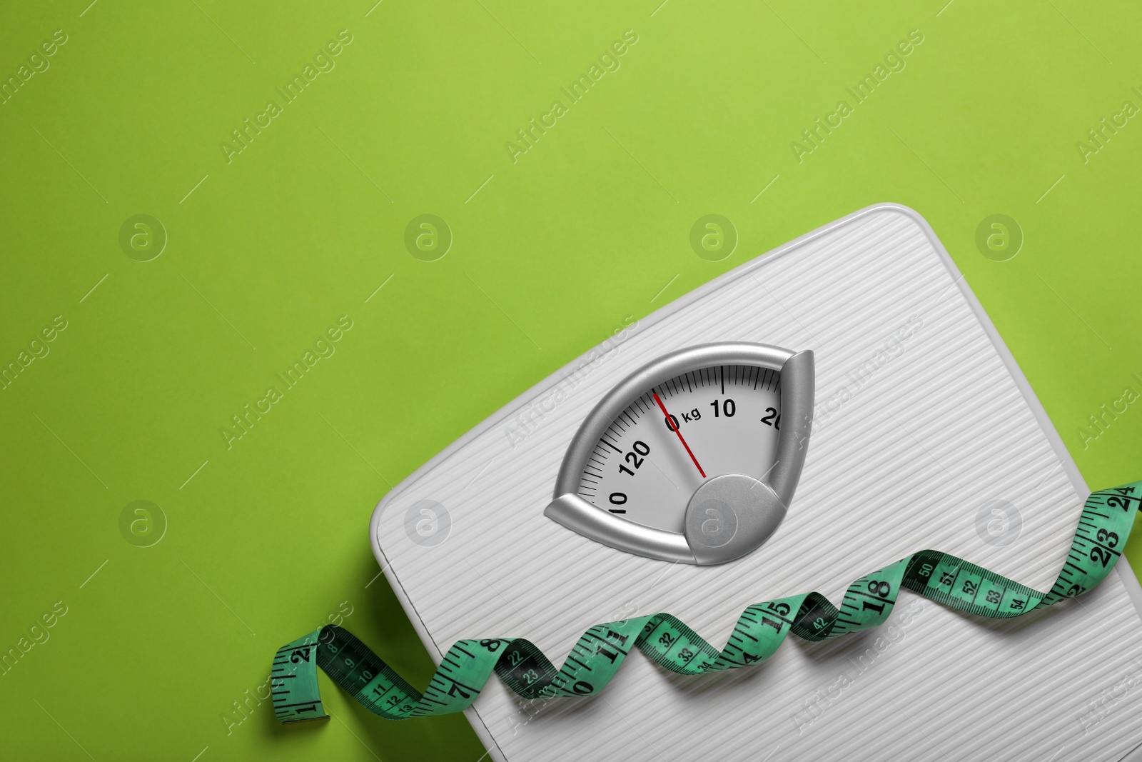 Photo of Weight loss concept. Scales and measuring tape on green background, top view. Space for text