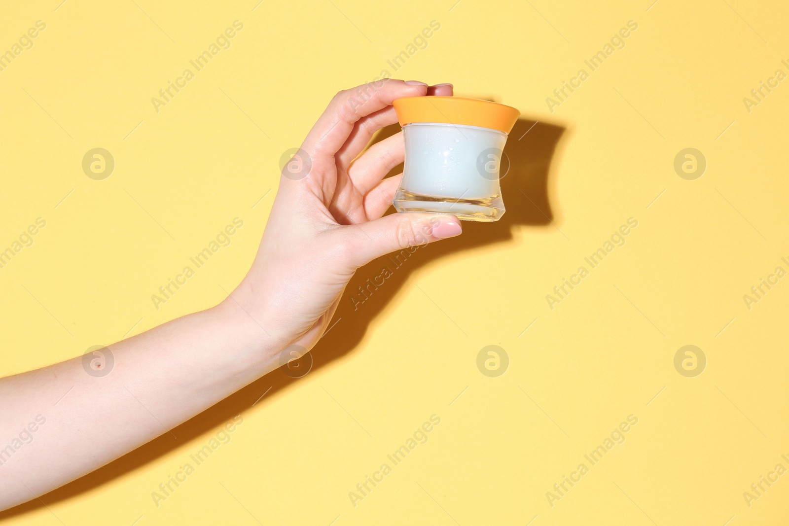 Photo of Woman holding jar of cream on yellow background, closeup