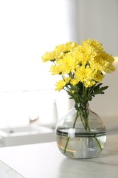 Vase with beautiful yellow chrysanthemum flowers on table in kitchen. Stylish element of interior design