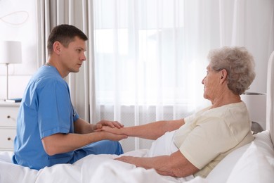 Photo of Caregiver talking to senior woman in bedroom. Home health care service