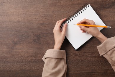 Photo of Woman writing in notebook at wooden table, top view. Space for text