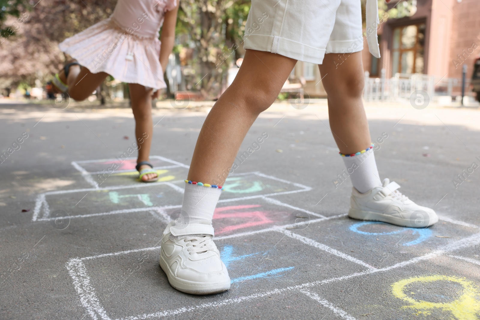 Photo of Little children playing hopscotch drawn with chalk on asphalt outdoors, closeup