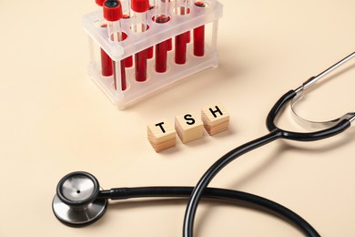 Photo of Endocrinology. Stethoscope, wooden cubes with thyroid hormones and blood samples in test tubes on beige background