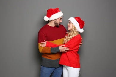 Young couple in Santa hats on grey background. Christmas celebration