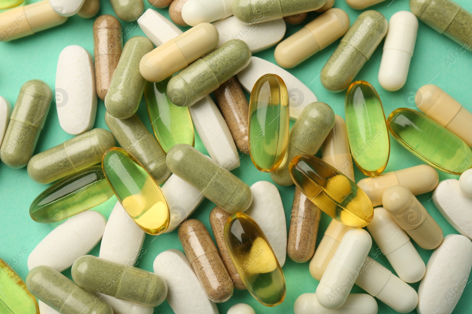 Photo of Different vitamin capsules on turquoise background, top view