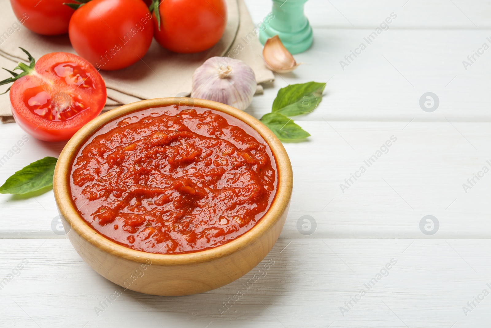 Photo of Homemade tomato sauce in bowl and fresh ingredients on white wooden table, space for text