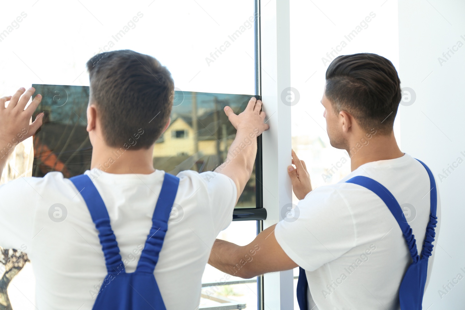 Photo of Professional workers tinting window with foil indoors