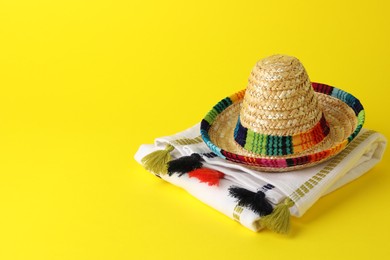 Mexican sombrero hat and poncho on yellow background, space for text