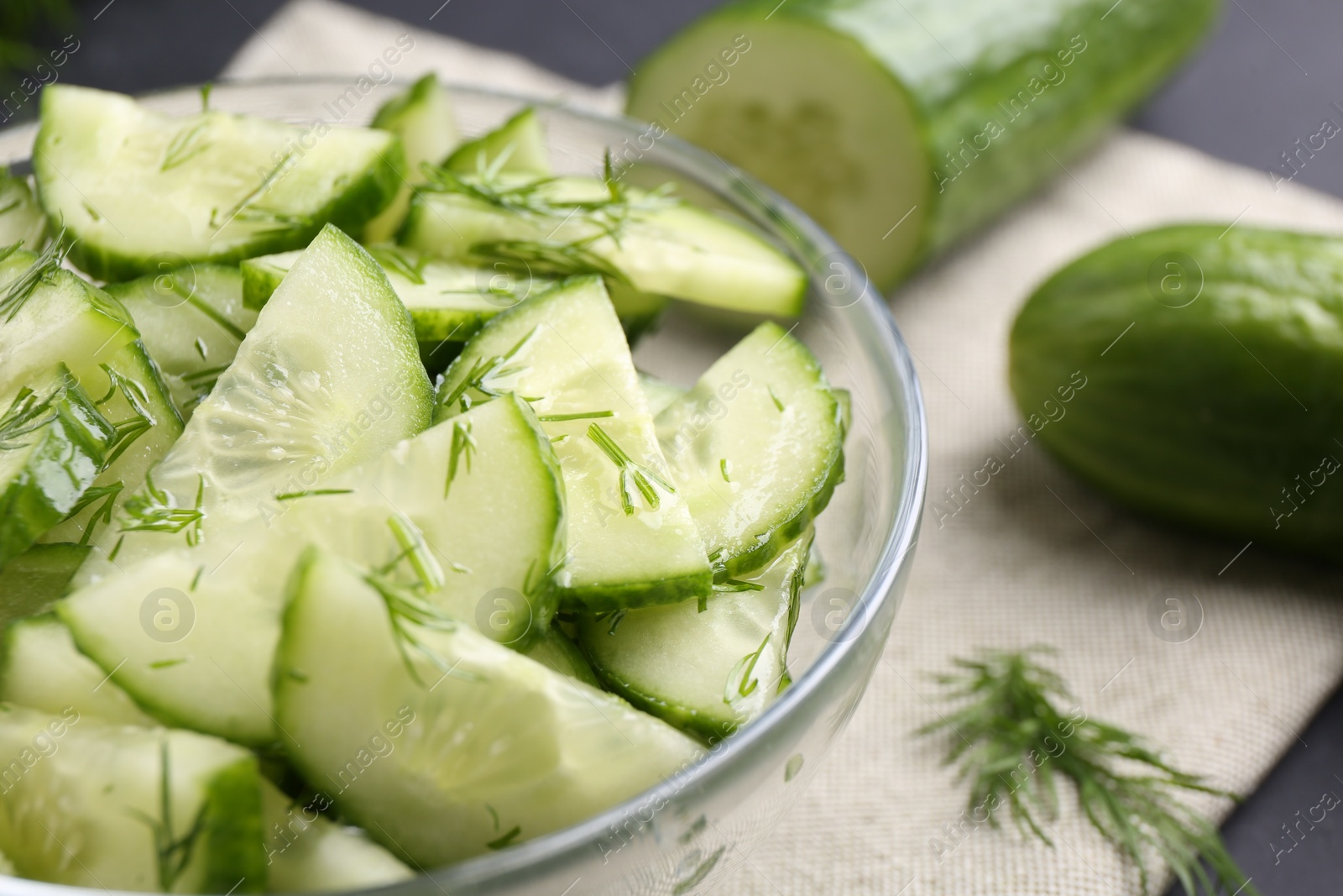 Photo of Cut cucumber with dill in glass bowl and fresh vegetables on table, closeup