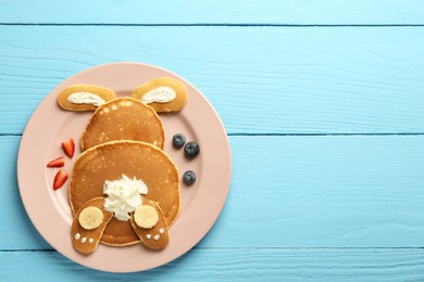 Photo of Creative serving for kids. Plate with cute bunny made of pancakes, berries, cream and banana on light blue wooden table, top view. Space for text