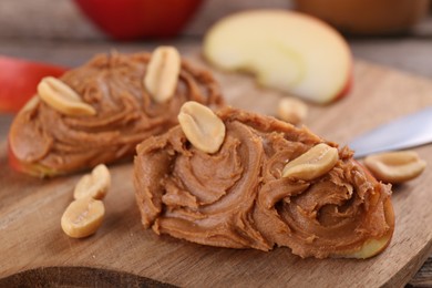 Photo of Pieces of fresh apple with peanut butter on wooden board, closeup