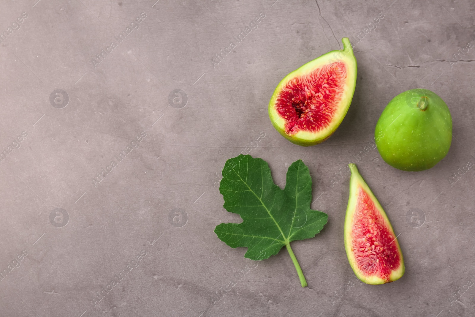 Photo of Cut and whole green figs with leaf on light gray table, flat lay. Space for text