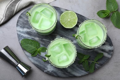 Delicious mint liqueur with ice cubes and green leaves on grey table, flat lay