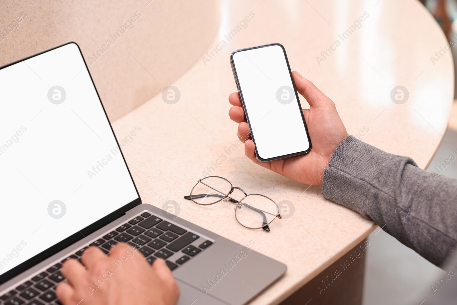 Photo of Man using smartphone and laptop at table in cafe, closeup