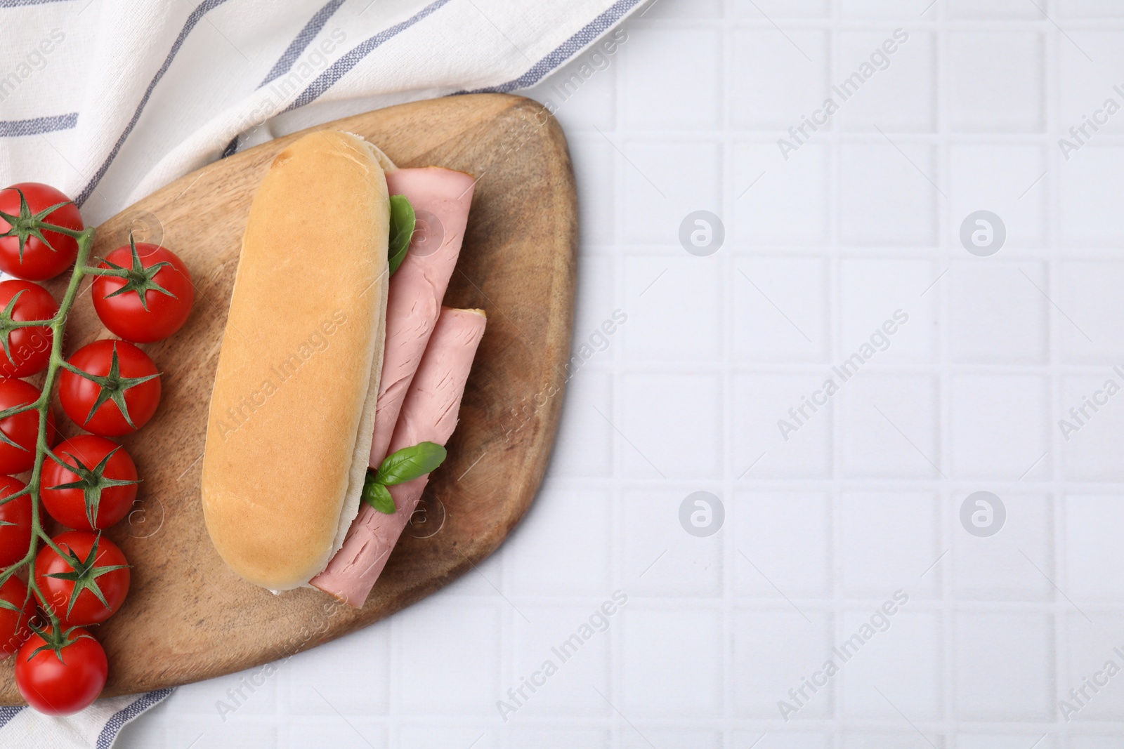 Photo of Delicious sandwich with ham, basil and tomatoes on white tiled table, top view. Space for text