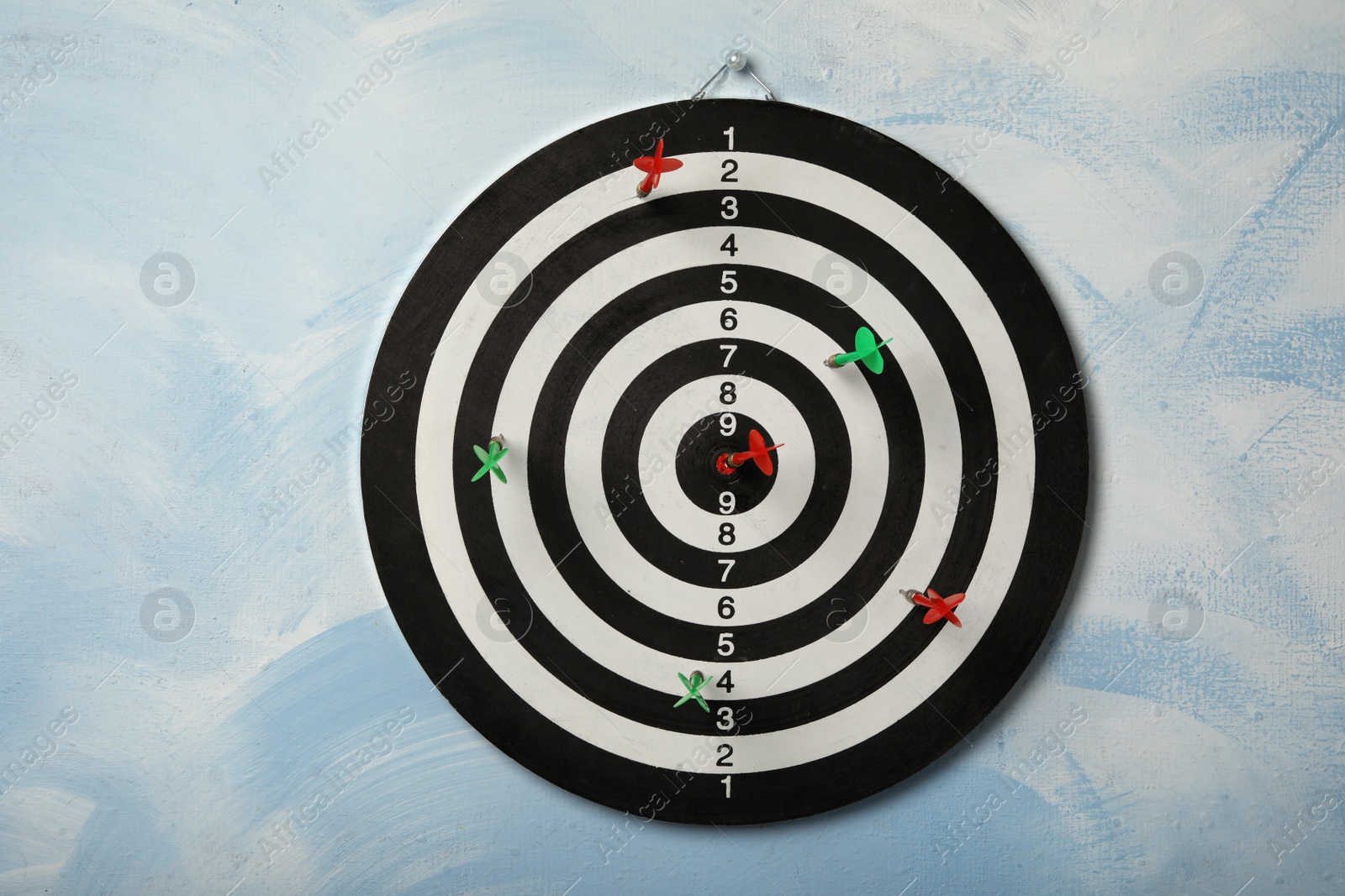 Photo of Arrows hitting dart board on light blue wall