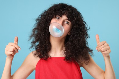 Photo of Beautiful young woman blowing bubble gum and showing thumbs up on light blue background