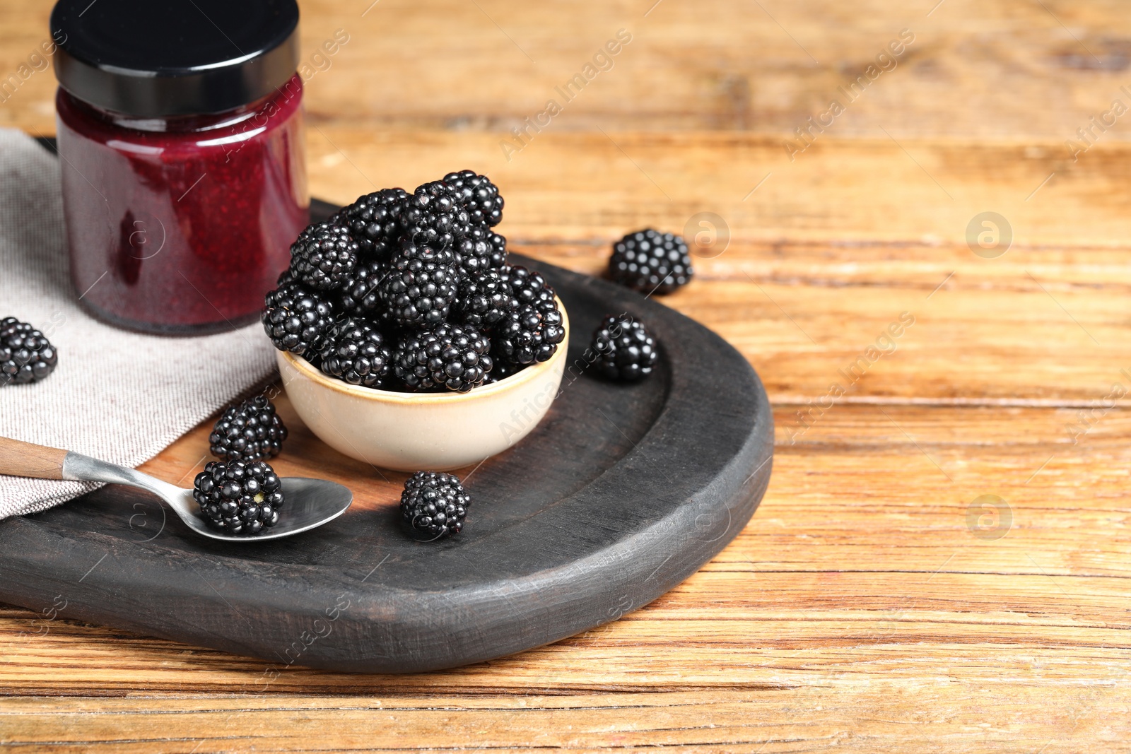 Photo of Fresh ripe blackberries and tasty jam on wooden table. Space for text