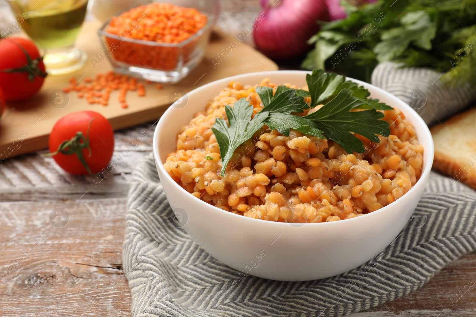 Photo of Delicious red lentils with parsley in bowl on wooden table, closeup