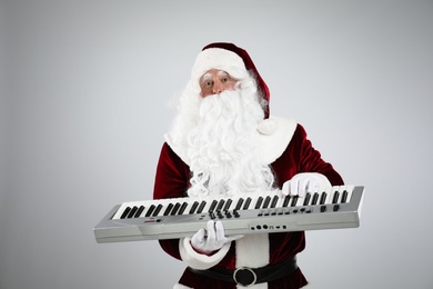 Photo of Santa Claus with synthesizer on light grey background. Christmas music