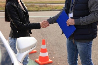 Photo of Young woman with instructor near car on test track, closeup. Driving school exam
