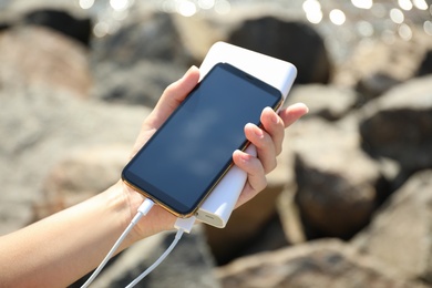 Woman charging smartphone with power bank on rocky mountain, closeup