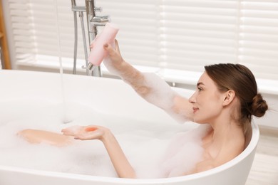 Photo of Woman pouring shower gel onto hand in bath indoors