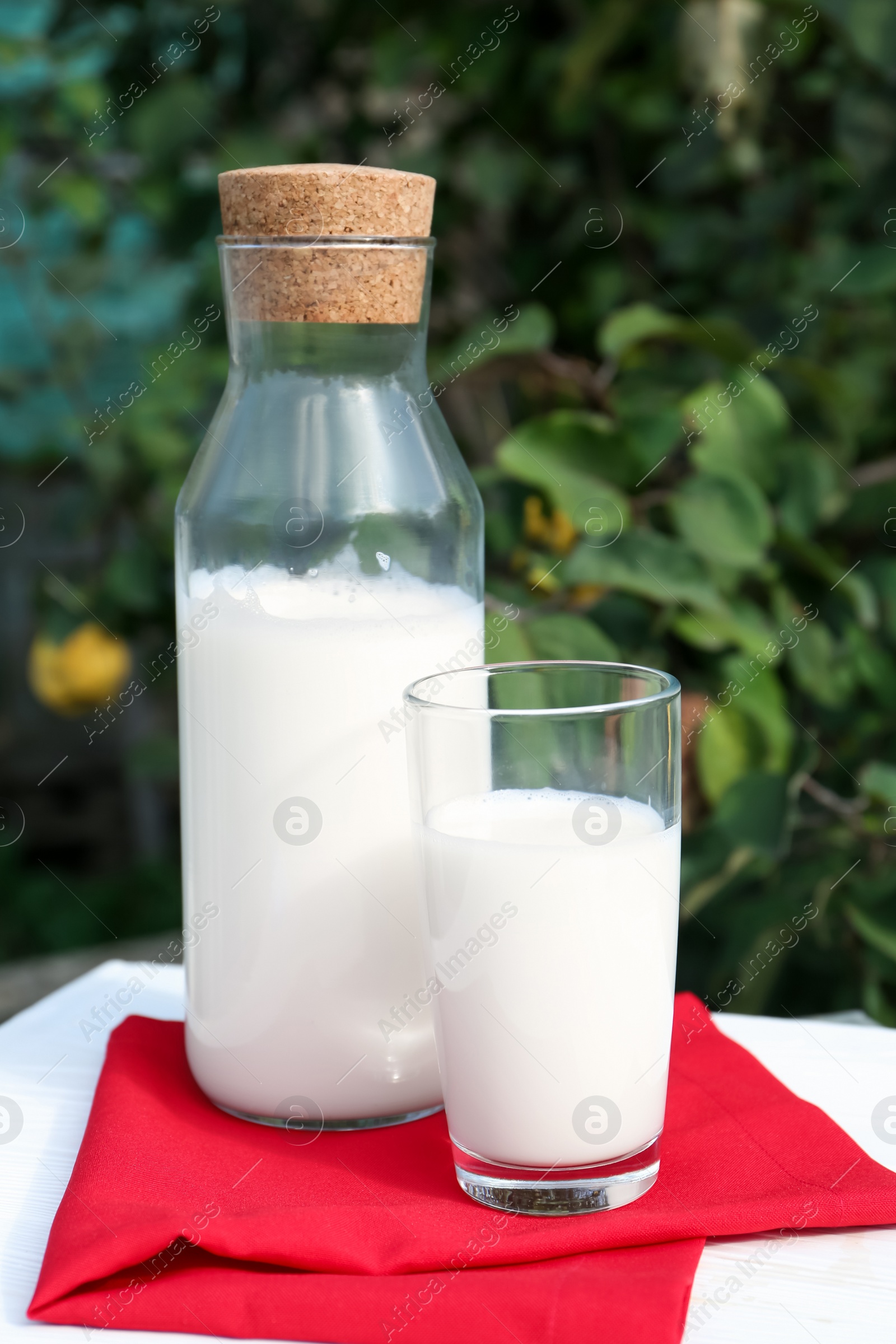 Photo of Glass and bottle of fresh milk on white wooden table outdoors