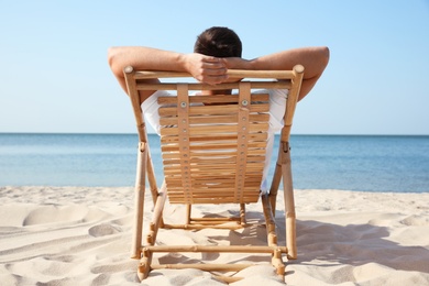 Photo of Young man relaxing in deck chair on sandy beach