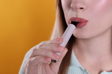 Photo of Young woman using electronic cigarette on orange background, closeup. Space for text