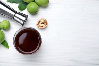 Photo of Delicious liqueur and fresh walnuts on white wooden table, flat lay. Space for text