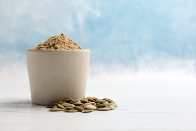 Photo of Bowl with pumpkin flour and seeds on table against color background. Space for text