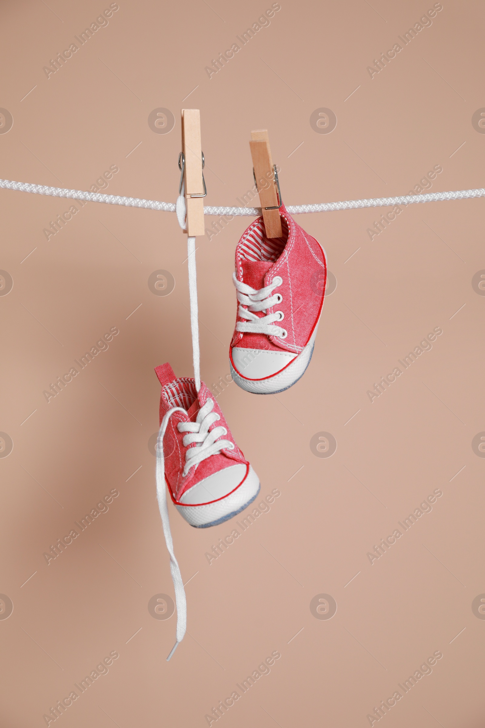 Photo of Cute small baby shoes hanging on washing line against brown background