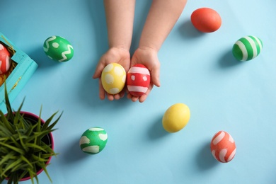 Photo of Little child holding painted Easter eggs on color background, top view