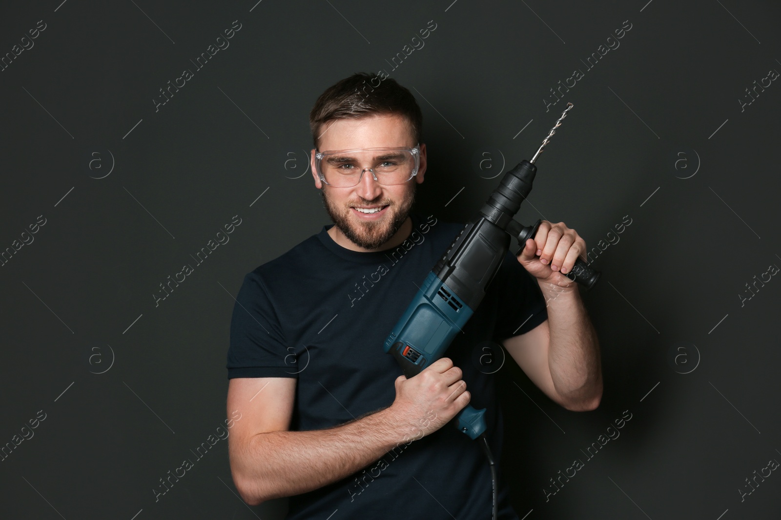 Photo of Young working man with rotary hammer on dark background