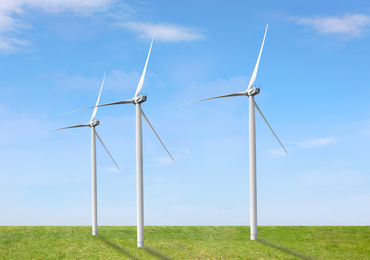 Image of Alternative energy source. Wind turbines in field under blue sky