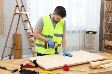 Photo of Young worker using electric drill at table in workshop