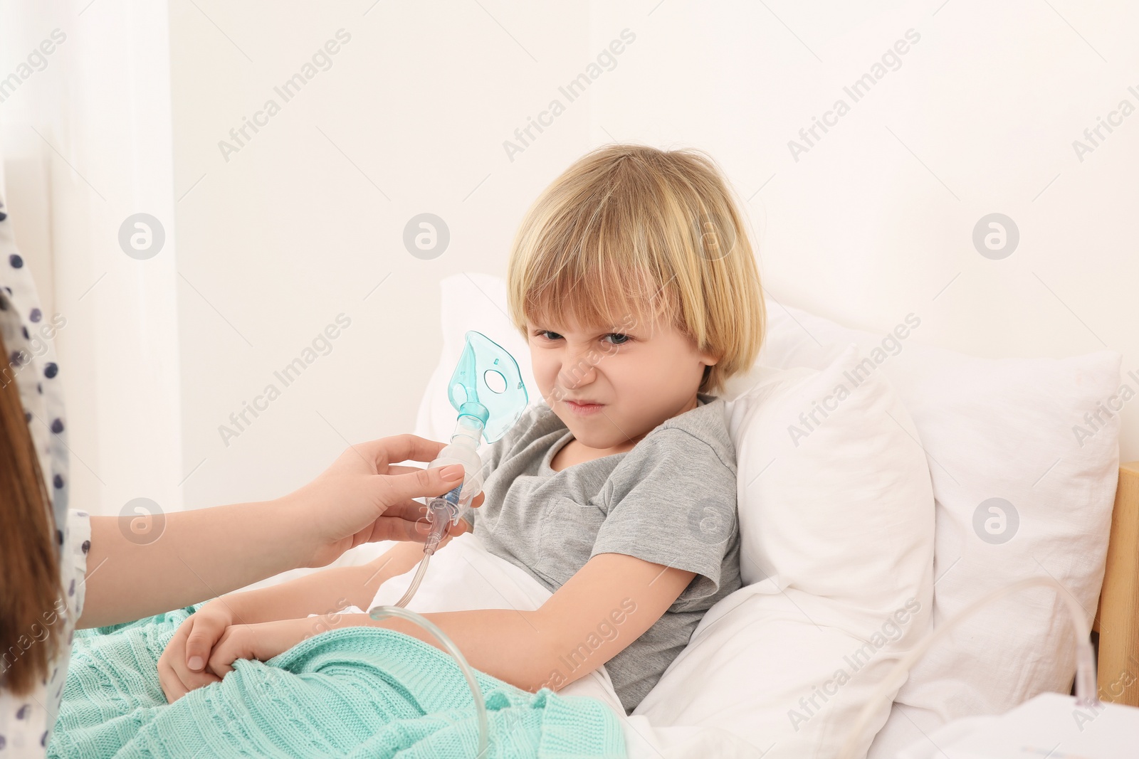 Photo of Mother helping her sick son with nebulizer inhalation in bedroom