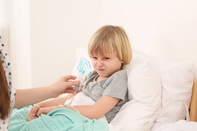 Mother helping her sick son with nebulizer inhalation in bedroom