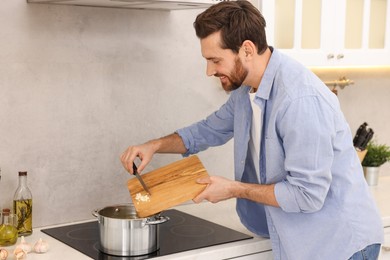 Photo of Man adding garlic into soup in kitchen