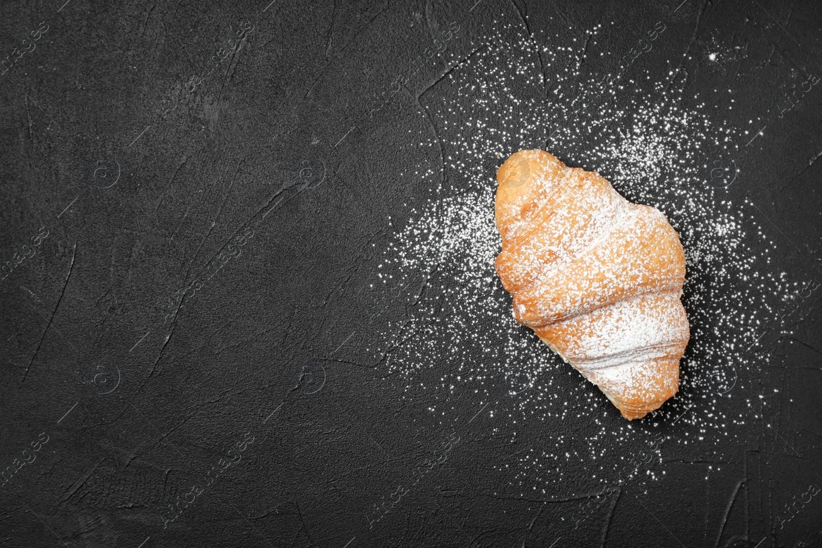 Photo of Tasty croissant with sugar powder on dark background, top view