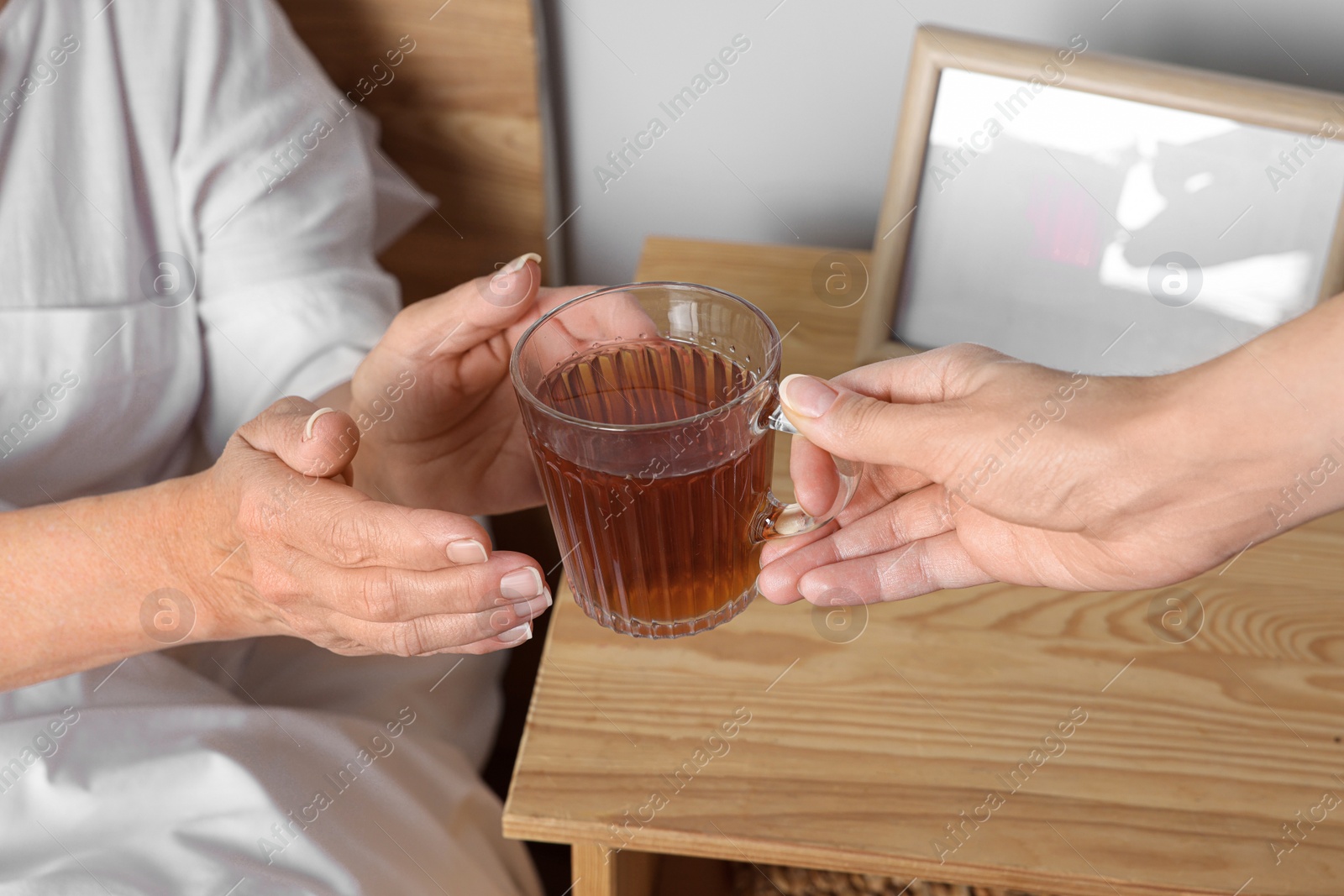 Photo of Caregiver giving tea to elderly woman at home, closeup