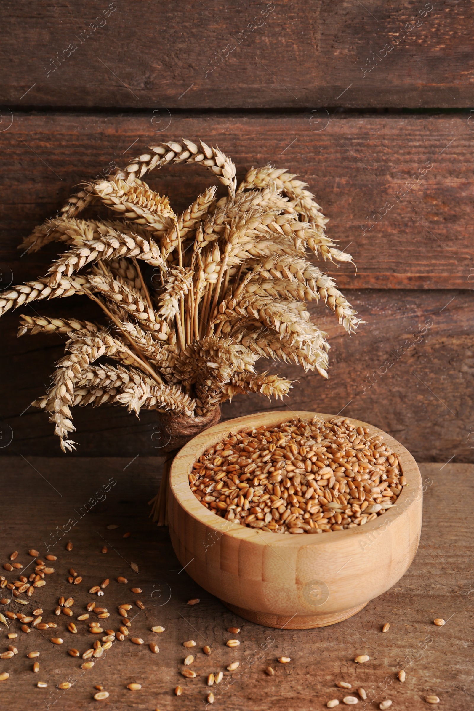 Photo of Wheat grains in bowl and spikes on wooden table