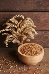 Photo of Wheat grains in bowl and spikes on wooden table