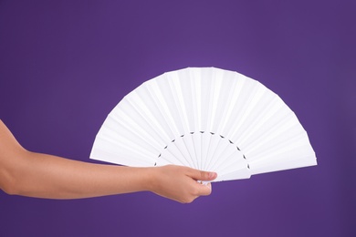 Photo of Woman holding white hand fan on purple background, closeup