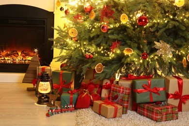 Photo of Many gift boxes, decorative elements and Christmas tree near fireplace at home